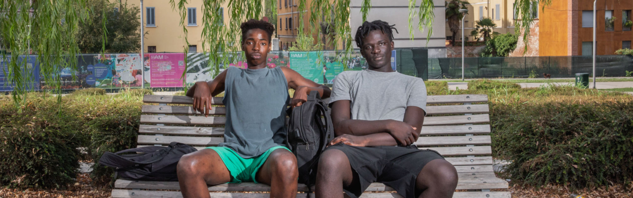 Ndongo Gueye, 18 anni, e Cheikh Badar Gueye, 19 anni, nati in Senegal e cresciuti nel nord Italia, siedono all'ombra della BAM Tree Library, un parco nel distretto finanziario di Milano. Italia, 2022 - Umidità 38%, Temperatura 35°C